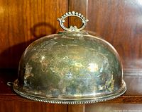 Photo showing front view of the silverplate meat dome with ornate handle and beaded edge with tarnish and scratches.