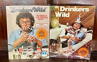 Photo showing both Smokers Wild and Drinkers Wild 1980s Avalon Hill board game boxes side by side, both unopened and with clear photographic covers.
