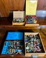 Four wooden jewelry boxes arranged on wood surface showing assorted jewelry inside.