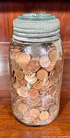 Full view of the large glass fruit sealer jar filled with Canadian pennies showing the metal lid and coins inside.
