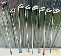Photo showing all golf clubs standing lined up, displaying RAM FX Black clubs including the irons and hybrids.