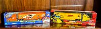 Two NASCAR diecast truck and trailer toys in original sealed packaging displayed side by side. One features Tony Stewart and Home Depot orange theme, the other features Kodak film yellow design.
