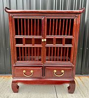 Front view of oriental style wooden cabinet with vertical slatted doors and two drawers with brass handles.
