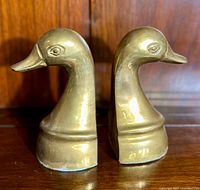 Pair of vintage yellow brass duck bookends side by side, showing the full profile of the duck heads and base design.