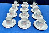 Overview of all 12 coffee cups placed on matching saucers arranged on blue cloth background.