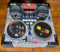 Front angled view of Yamaha DJX-IIb showing top panel controls, two speakers, central display, large circular control plates with labeled functions, and various knobs and buttons.