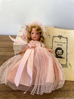 Front view of the vintage Storybook Doll bridesmaid wearing a pink tulle dress with satin ribbon and flower, with molded blonde hair and original booklet behind.