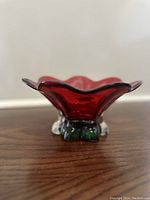 Side view of the translucent red flower-shaped glass bowl showing wavy edges and green base