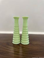 Pair of two tall ribbed Jadite green glass bud vases standing upright on wooden surface, showing shape and texture.