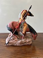 Side angle showing Native American warrior figure with spear on horse atop a rock-like base.