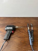 Photo of Weller soldering gun and two handheld soldering irons laid on wooden surface