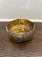 Side view of brass bowl on wood surface showing scalloped rim and hammered texture.