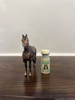 Small bronze horse figurine beside a small bottle for size comparison, showing front and detail view
