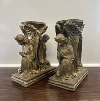Side angled view showing two vintage angel resin candle holders on wood surface, highlighting intricate wing and robe details.