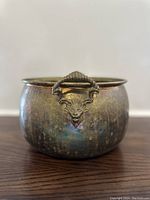 Front view of brass jardinière showing one of the lion head handles with ring mouth