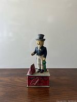 Front view of vintage cast iron Uncle Sam mechanical bank on wooden surface with plain background.