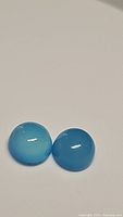 Pair of round cabochon bright blue chalcedony gemstones shown on a white background