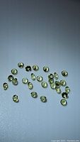 Overview of small round apple green Peridot gemstones spread out on a light surface, showing color and cut.