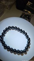 Close-up photo of a natural hematite 8mm bead stretchy bracelet lying flat on a plain surface.
