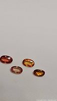 Four oval cut natural fancy colored sapphires on a white background. Colors include reddish-orange, yellow-orange, lighter orange-pink, and deep orange.