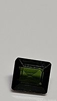 Close-up image of rectangular emerald cut green Tourmaline gemstone showing facets and luster.