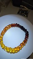 Photo showing full circular stretchy bracelet with polished Baltic amber beads in gradient from yellow to dark brown on white background.