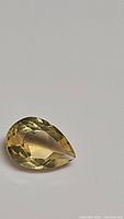 Natural pear-shaped citrine gemstone with yellow color and faceted cut shown on a neutral background.