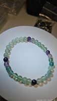 Photo of the natural fluorite beaded bracelet laid flat showing round, smooth gemstone beads in green, purple, and translucent colors.