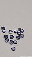 Multiple natural purple iolite round cabochon gemstones on a neutral grey surface showing their translucent purple color and smooth dome shape.