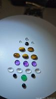 Polished natural gemstones illuminated to show colors, shapes, and clarity, arranged in rows on white background.