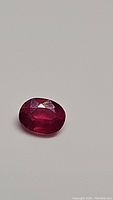Loose oval cut red ruby gemstone on white background, showing overall shape and color.
