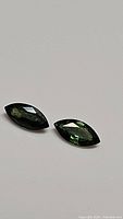 Two marquise-cut green sapphires on plain background