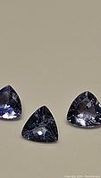 Three natural tanzanite gemstones in trillion cut, showing strong purple-blue color and faceted surfaces.
