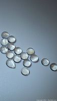 Photo showing multiple small polished white moonstone cabochons displaying a catseye effect in a loose parcel.