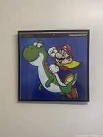 Front-facing photo of framed 12x12 Nintendo artwork showing Mario and Yoshi on blue background, with Nintendo and Super Mario World 1992 titles visible.