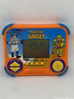 Front view of handheld game showing screen and controls with Inspector Gadget graphics.