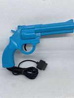 Front angled view of blue plastic revolver style light gun with attached cable.