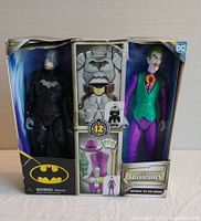 Front view of the retail box showing Batman and Joker figurines inside along with accessory slots and damage to the box.