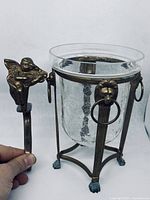 Close-up showing brass angel coat hook held by hand next to the brass glass holder structure