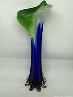 View of glass vase angled to show ruffled green rim, blue to clear gradient body, and decorative base