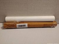 Two rolled posters atop a flat surface, one wrapped in plastic brown packaging and one white.