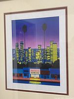 Framed print showing the full artwork within a brown frame, the art includes a night cityscape with two palm trees and a record store with lit signage.