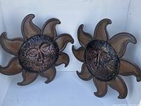 Two metal sun face wall pieces displayed side by side showing their full shape and texture.