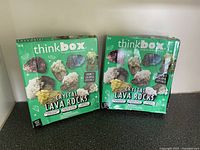 Photo shows two ThinkBox Crystal Lava Rocks kit boxes side by side, each featuring images of colorful crystals growing on lava rocks. Boxes green with pictures of various crystals.