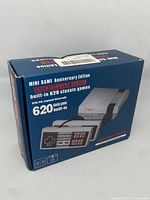 Box front of Mini Game Anniversary Edition console showing 620 built-in classic games and image of console and controllers.