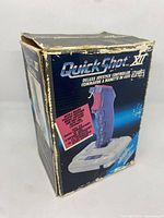 Photo of the original box for Quick Shot XII Deluxe Joystick controller for NES showing front and side with product branding and condition wear.