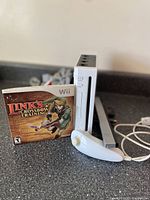 White Nintendo Wii console standing vertically with Link's Crossbow Training game case and white Nunchuck controller on counter.
