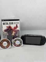 Photo showing the Sony PSP 1001 console, Metal Gear Ac!d game case, and two UMD discs including Metal Gear Ac!d and Midnight Club 3 DUB Edition Remix.