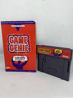 Photo of the Game Genie cartridge and the original Game Genie Code Book in used condition.