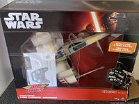 Front boxed view of Star Wars Air Hogs X-Wing Starfighter drone showing packaging and included manual and remote control.